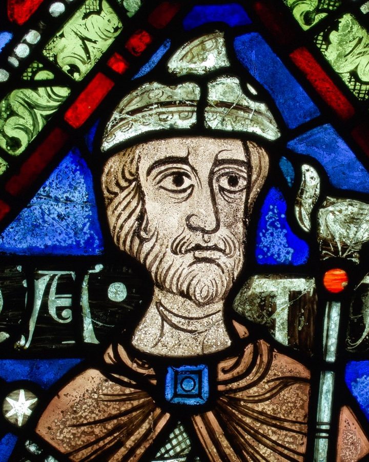 Medieval stained glass portrait of a bearded figure in a cap, framed in red, blue and green glass
